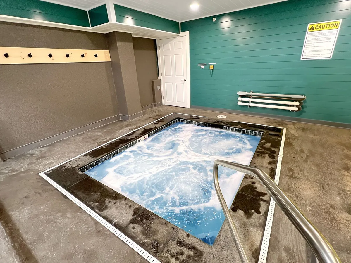 The tranquil interior whirlpool spa features soothing teal walls, a stainless steel handrail, and bubbling water—an inviting place for relaxation and wellness routines.