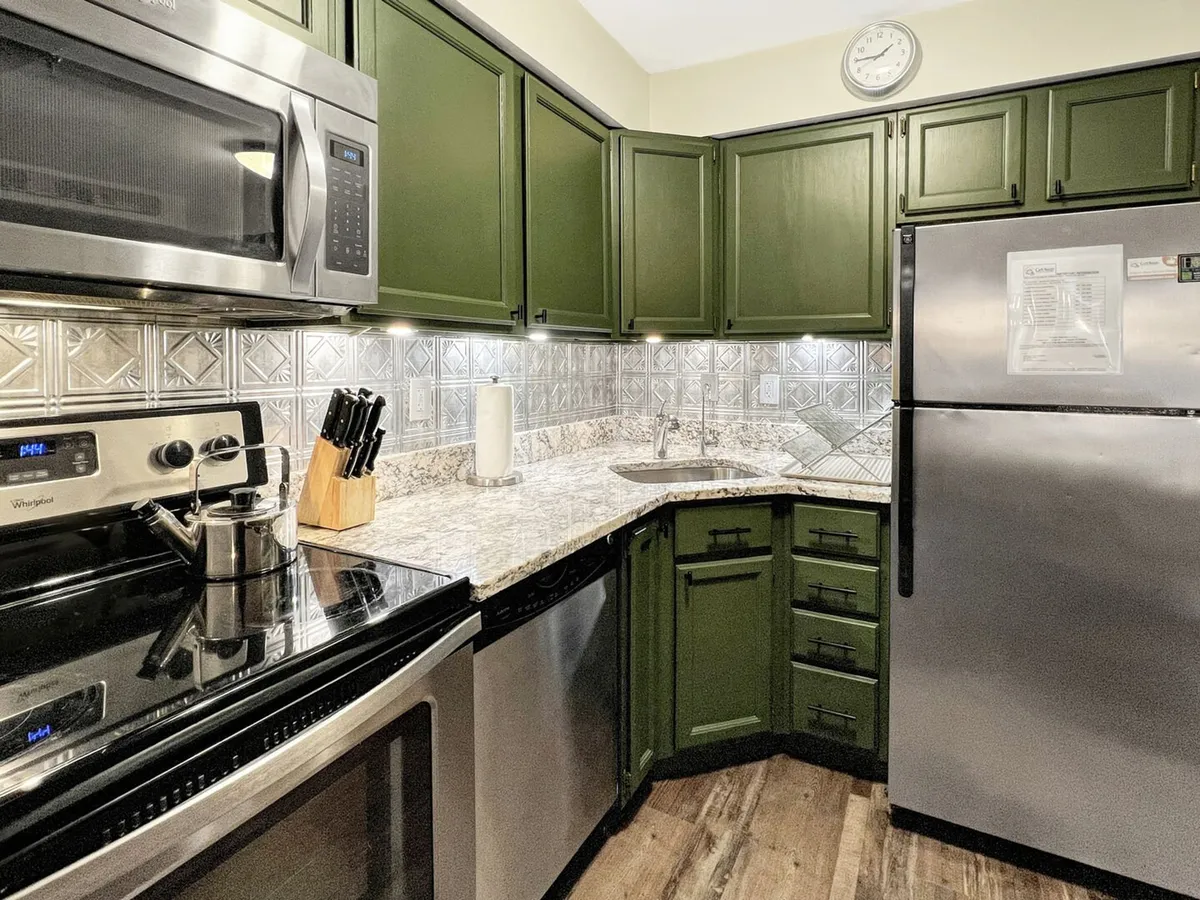 A modern, chef-ready kitchen equipped with stainless steel appliances, green cabinets, decorative tile backsplash, and ample granite countertops. The space is bright, functional, and perfect for cooking feasts or preparing après-ski snacks.