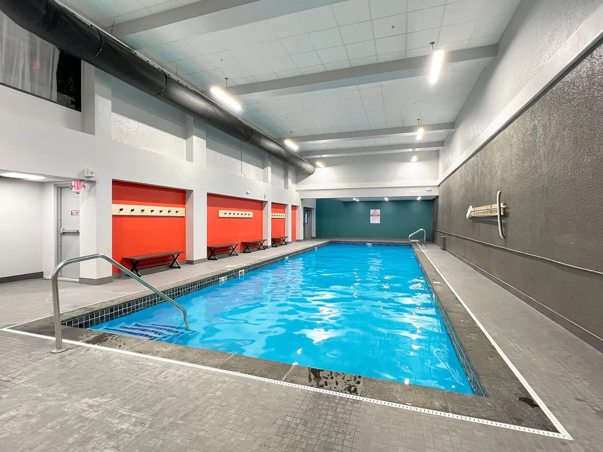 This interior image showcases the bright indoor swimming pool with a vibrant red accent wall, benches along the side, and clear, inviting water. The atmosphere is energetic and rejuvenating, supporting swimming, relaxation, and socializing year-round.
