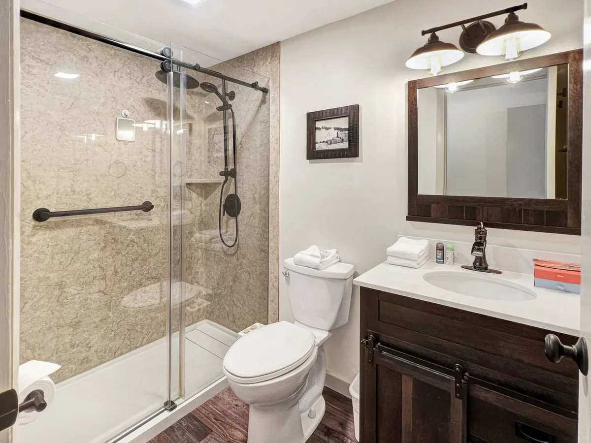 A modern bathroom with a glass shower enclosure, dark wood vanity, framed mirror, and elegant bathroom accessories. The space is bright and inviting, suggesting a fresh start to each day or a relaxing wind-down in the evening.