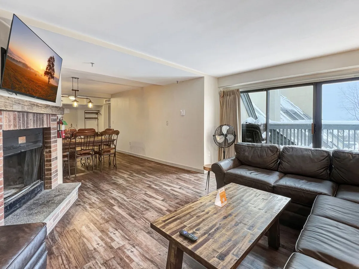 A warm and inviting open-concept living and dining area featuring a cozy fireplace, a plush sofa, a dining table for group gatherings, and a wall-mounted flat-screen television. The space is enhanced by alpine-inspired decor and soft lighting, creating an ideal setting for relaxation and connection.